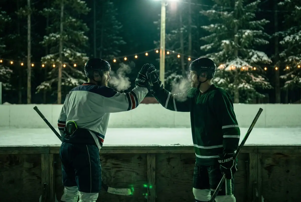 Two rec hockey players high-fiving at the boards under a floodlight